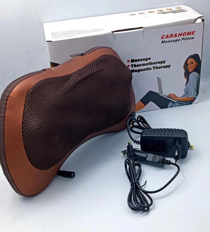 Massage pillow with brown surface and black mesh, accompanied by its power adapter and cable, on a white background.